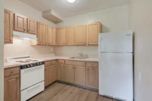 Interior Unit Kitchen, White appliances, wood like flooring, light brown wood cabinetry, stainless steel sink.
